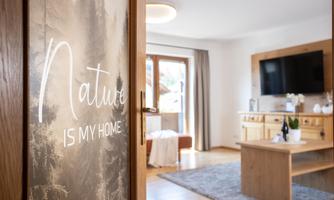 A cozy living space with a large television and wooden interior. The door features the inscription “Nature IS MY HOME”.