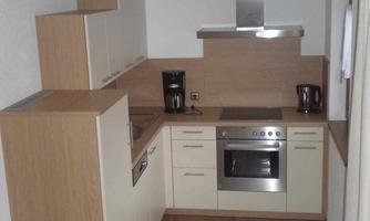 A modern kitchen with wooden and white furniture. It is equipped with a stove, a range hood, and kitchen appliances.
