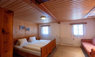 A cozy room with two single beds and wood paneling. A sofa and windows with curtains create a warm atmosphere.