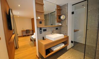 A modern bathroom with a sink made of white stone and wooden shelves. The area is bright and well-lit, featuring an elegant glass shower.