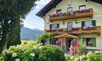 Hubertus Apartment House, decorated with colorful flowers. In the foreground, white hydrangeas are blooming, and the mountains are visible in the background.