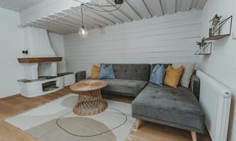 A stylish living room with a gray sofa and colorful cushions. The room features wood-paneled walls and a rustic fireplace.