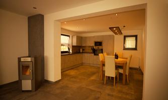A modern kitchen with light furniture and a large dining table. On the left side, there is an oven, and the walls are in neutral colors.