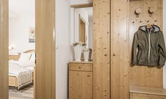 A bright hallway with a wooden piece of furniture that includes a wardrobe and cabinets. In the background, a bedroom is visible.
