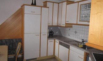 A modern kitchen with bright wooden cabinets and a clear arrangement. Some kitchen utensils are on the countertop and a table is placed beside it.