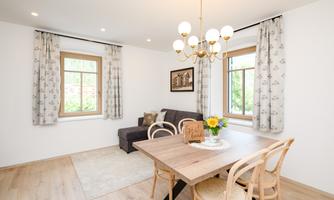 A cozy living space with a dining table and chairs. Large windows and bright walls create an inviting atmosphere.