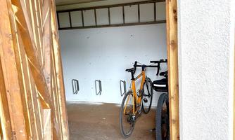 A bicycle stands in a simple storage room with wooden paneling. The walls are bare, and the room appears well-organized.