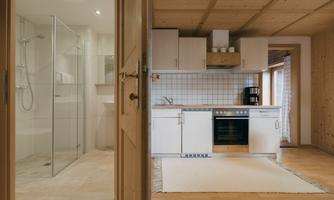 A modern kitchen with bright wood elements and a shower stall in the background. The room is well lit and feels inviting.