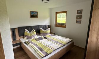 A cozy bedroom with a double bed and colorful cushions. A window provides ample daylight and a pleasant atmosphere.
