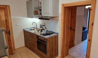 A modern kitchen with wooden shelves and a stove. From the kitchen, there is access to both the bedroom and the living room, as well as the bathroom.