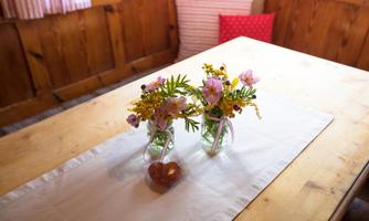 A table with two small glass vases filled with colorful flowers. Beneath it lies a white tablecloth and a heart-shaped decor element.