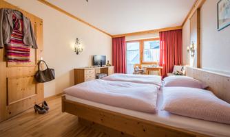A cozy bedroom with two beds and a wooden furniture design. Daylight streams through the window onto the warm atmosphere of the room.