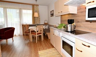 A bright and modern kitchen with a dining table and chairs. The room has large windows and warm wooden floors.