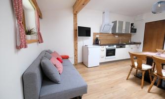 A modern kitchen with a dining area and a cozy couch.  
Bright wooden floors and windows with curtains create an inviting atmosphere.