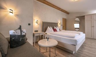 A modern bedroom with two single beds and a cozy sitting area. The room is bright and stylishly decorated, with warm lighting and beautiful wall paneling.