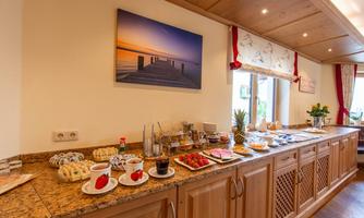 An inviting breakfast setting with a variety of foods and drinks on a wooden counter. In the background, there is a picture of a sunset over a dock.