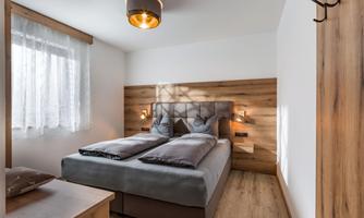 A modern bedroom with a double bed and wooden elements. The room is bright and friendly, with a large window and warm lighting.