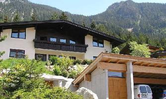 A beautiful house in the mountains with a wooden balcony. Surrounded by green trees and impressive mountain peaks.