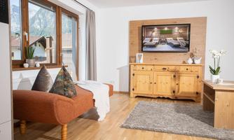 A cozy living room with a brown sofa and decorative pillows. A television and a wooden furniture piece complement the warm atmosphere.