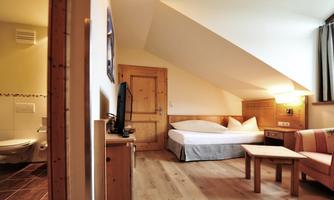 A cozy room with slanted walls and wooden furniture. There is a bed, a television, and a seating area.
