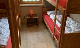 A simple room with two bunk beds and red bedding. There is a small table and a window that lets in a lot of light.