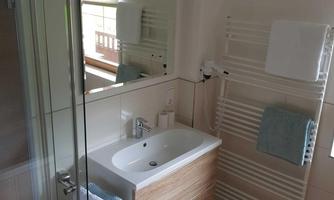 A modern bathroom with a glass shower and a wooden sink. Towels and a warm rug complete the cozy atmosphere.
