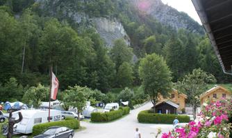 A beautiful campsite nestled among trees and mountains. There are RVs and small cabins along the road.