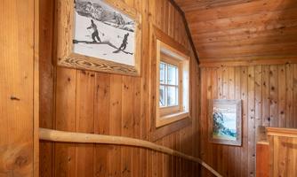 A wooden-paneled staircase with windows and pictures on the wall. The atmosphere feels cozy and inviting.