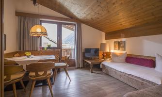 A cozy room with a wooden ceiling, a dining table, and a television. Large windows offer a view of the mountains.