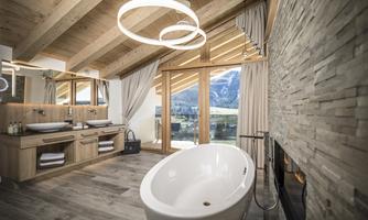 A modern bathroom with a freestanding bathtub and large windows that offer a view of the mountains. The interior is made of wood, with stylish light installations.
