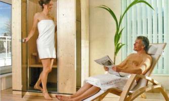 A sauna with a woman who is just coming out and a man who is relaxed on a lounge chair. The room has a bright, inviting atmosphere with large windows and plants.