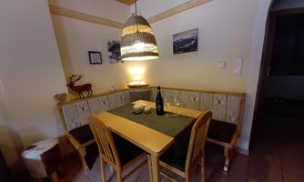 A cozy dining area with a wooden table set and a bench. A bottle of wine is on the table and decorative objects are spread around the room.