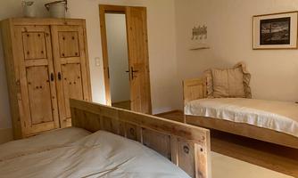 A cozy bedroom with two wooden beds and a wardrobe. The walls are light and the room is well lit.