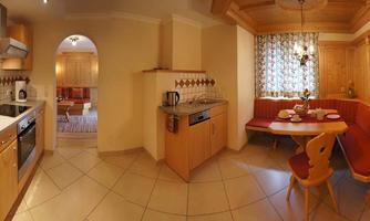 A modern kitchen with wooden furniture and a dining area. The room is bright and friendly, with a beautiful window curtain.