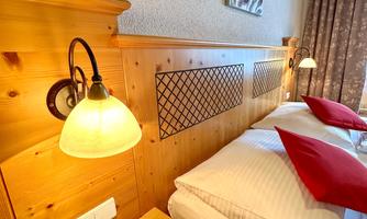 A cozy bedroom with wooden furniture and red pillows. Warm light from the lamps creates an inviting atmosphere.