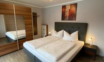 A modern bedroom with a large bed and two pillows. The room features a mirror and a cozy atmosphere.