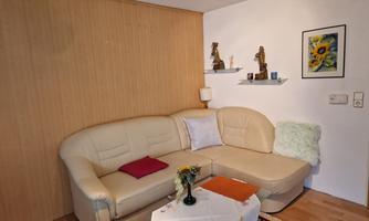 A cozy living space with an L-shaped couch and a small table. Some decorations and a floral painting hang on the wall.