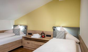 A cozy room with two single beds and a modern wooden dresser. The wall is painted in a soft yellow, creating an inviting atmosphere.