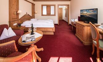 A cozy hotel room with wooden furniture and a red carpet. It includes a double bed, a TV, and a small table with chairs.