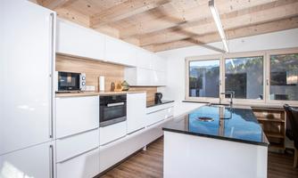 A modern kitchen with white cabinets and a cooking island. Large windows provide plenty of daylight.