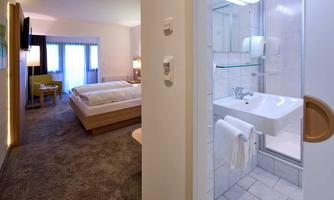 A modern hotel room with a double bed, a television, and a desk. The bathroom is bright and clean, with a shower and a sink.