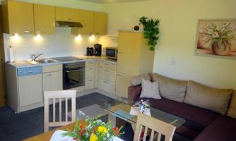 A modern kitchen with a dining area and a cozy living room. The furniture is bright and cheerful, and there are fresh flowers on the table.