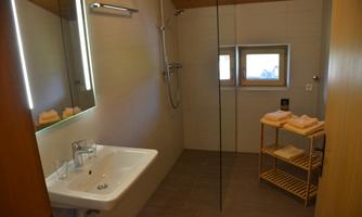 A modern bathroom with a shower, a sink, and a large mirror. Fresh towels are ready on a wooden shelf.