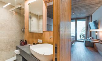 A modern bathroom with a freestanding bathtub and elegant wooden details. In the background, a room with a view and a TV is visible.