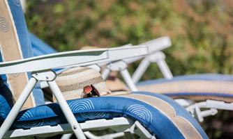 Two lounge chairs with blue and beige cushions are outside. A straw hat and sunglasses are resting on one of the chairs.