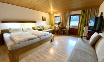 A comfortable room with two beds, a sofa, and a table. Large windows offer a view of the surroundings and provide plenty of light.
