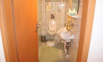 A small bathroom with a toilet, sink, and green bath mat. The walls are tiled and there are some bathroom utensils on a shelf.