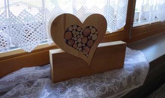 A decorative wooden heart with small wooden discs is placed on a windowsill. The atmosphere is bright and friendly due to the window decoration.