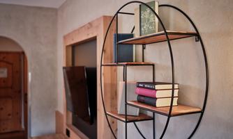 A modern wall shelf made of metal and wood with several stacks of books. In the background, a television is visible.