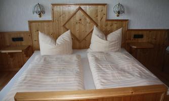 A cozy bedroom with a wooden bed and large, pointy pillows. The walls are clad in wooden panels, and there are nightstands with lamps.